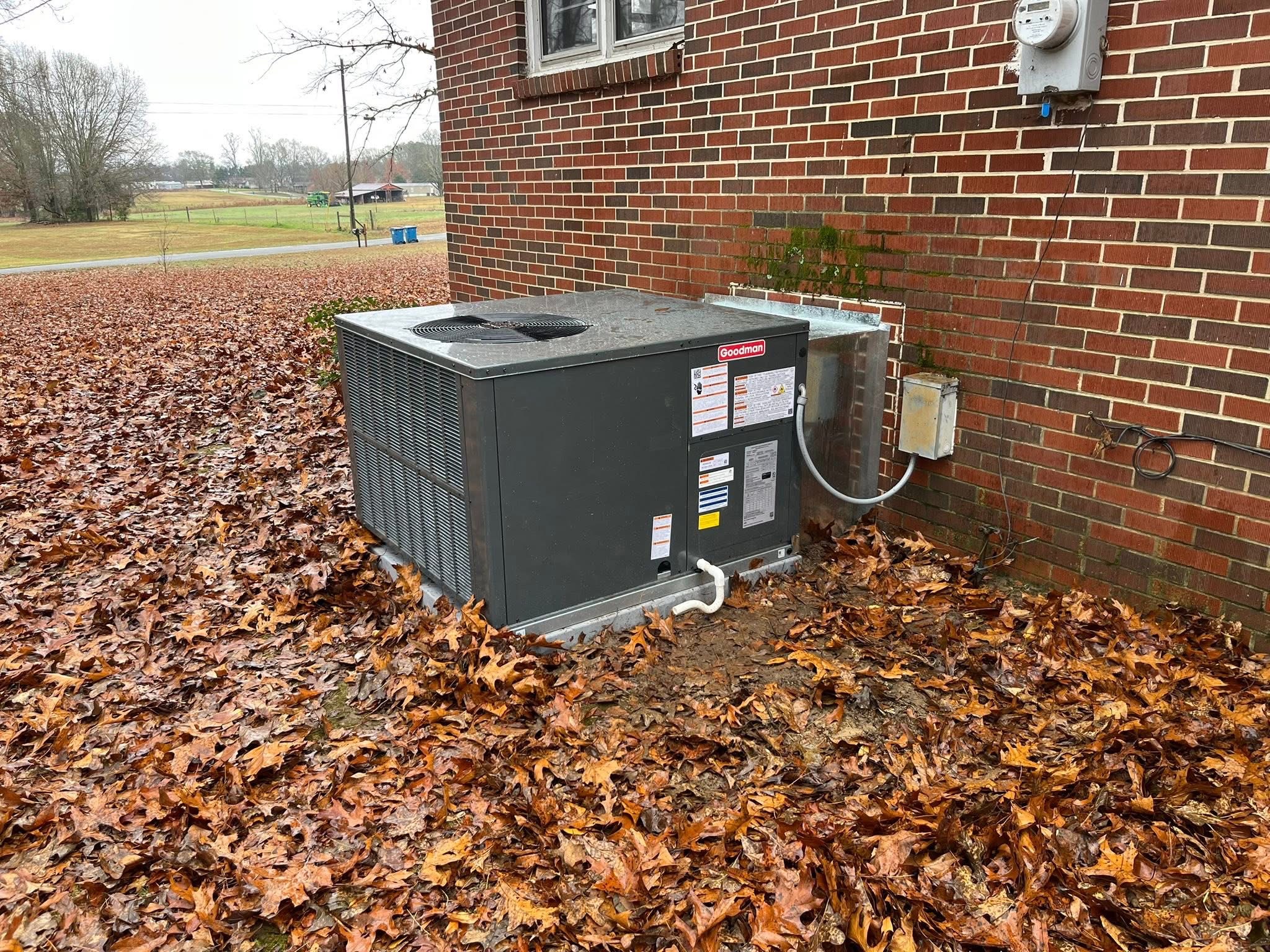 New Goodman package unit installed on a fresh pad beside the same brick house